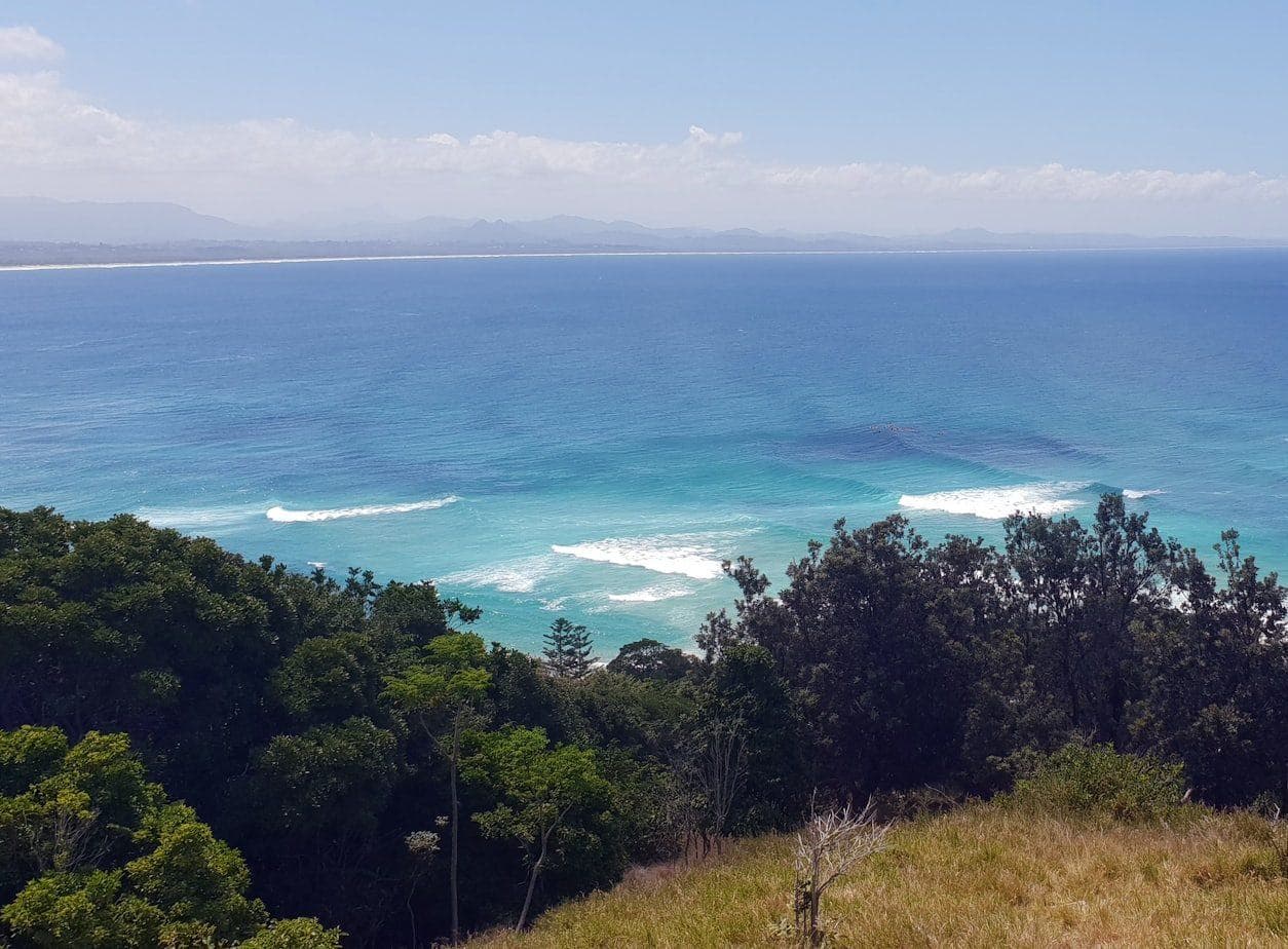 Looking north from the headland at Cape Byron: surf breaking on a long beach, with the caldera ranges blue on the horizon.
